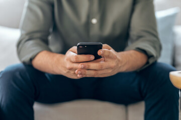 Hands of business man using smartphone texting while relaxing on sofa at home.