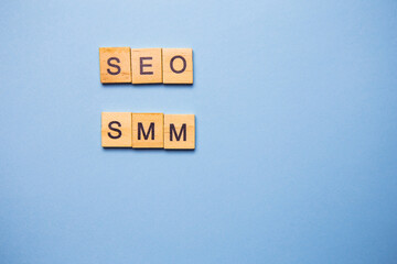 Wooden letters SEO and SMM are printed on a light blue background.