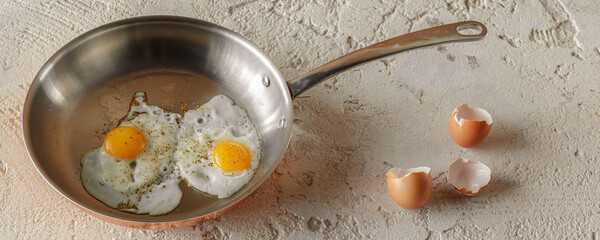 Two fried eggs in copper pan and egg shells on rough textured clay background. Healthy breakfast concept.
