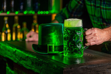 Male hand with mug of green beer, ale on the bar counter. Holiday of Ireland on St. Patrick's Day in irish pub, bar. Festive Leprikon's green hat. National tradition of carnival celebrating March 17