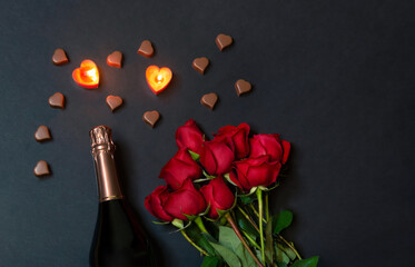 Valentine's day concept. Red roses, bottle of champagne, burning candles and chocolate candies.