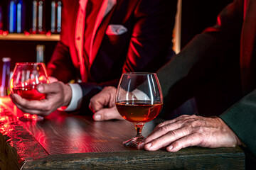 Man's hands with brandy glass on the bar counter. Alcoholic beverage, cognac, whiskey, port, brandy, rum, scotch, bourbon. Vintage wooden table in the dark