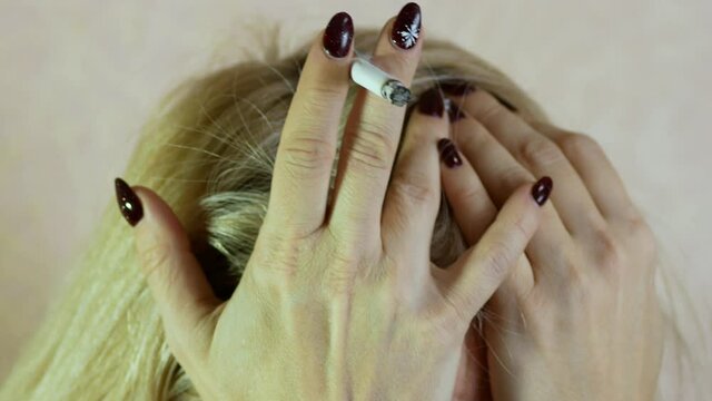 Upset blonde woman with a cigarette clutched her head with her hands being depressed. Sad Caucasian woman emotionally experiencing loss and stress. Selective focus