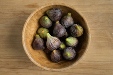 Obraz premium Top view figs in wooden bowl on wooden table, with copy space. High quality photo