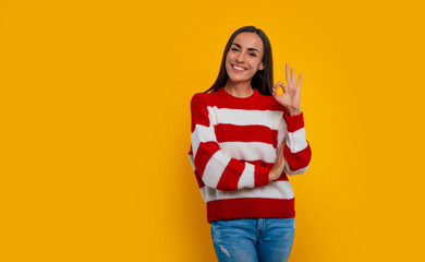 Everything fine! Smiling cute young brunette girl shows an ok sign on the camera in studio © My Ocean studio