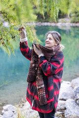 Happy smilling woman posing playing with tree branches. Natural clean blue lake background. Natural lighting. Warm autumn clothes.