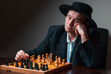 Portrait of professional chess player, posing with board staring at camera. Classical formal suit, vintage look. Competitive strategy game.