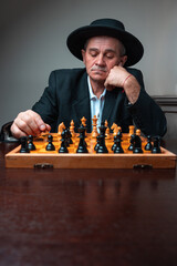 Portrait of man with hat focused on chess board. Classical formal suit, vintage look. Concentrated player, thinking of strategies.