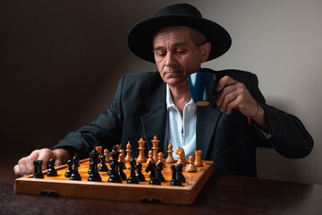 Portrait of chess player drinking coffee while playing with himself, thinking of new strategies. Classical formal suit, vintage look. Competitive strategy game.