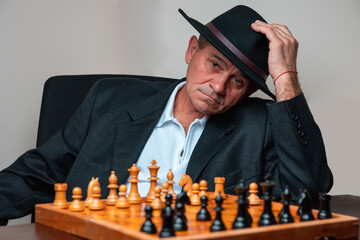 Portrait of man sitting, tipping his hat. Classical formal suit, vintage look. Chess table invite, waiting for players.