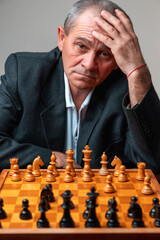 Portrait of professional chess player, posing with board staring at camera, holding his head. Classical formal suit, vintage look. Competitive strategy game.