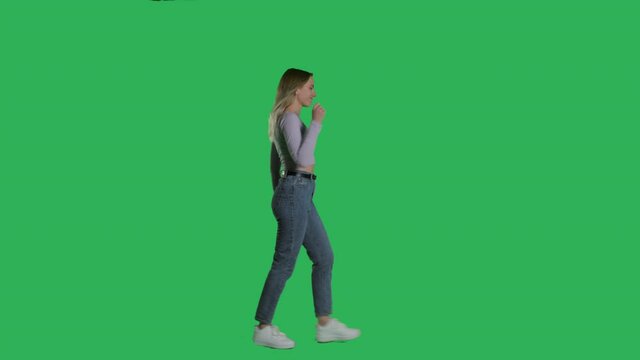 Woman in white t-shirt, jeans and sneakers walking on a Green Screen, Chroma Key. 4k UHD side view isolated video.