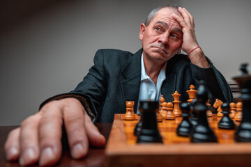 Portrait distracted man playing chess match, holding head with his hand looking to the side. 
Classical formal suit, vintage look. Professional challenge, struggling thinking of strategy.