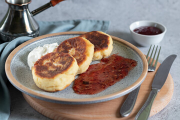 fried cottage cheese pancakesonand jezve on a wooden board with grey textiles