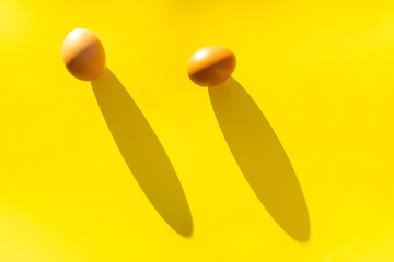 Two brown farm eggs on a yellow background in bright light, a concept of minimalism