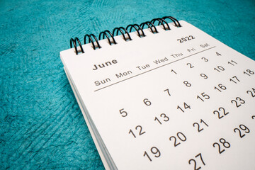 June 2022 - spiral desktop calendar against green handmade paper, low angle macro shot, time and...