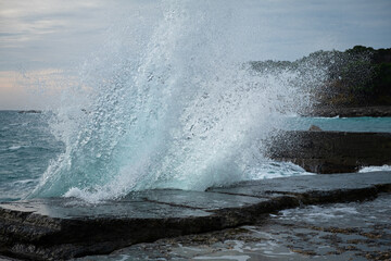 Turquoise sea stone beach, breaking waves on a cloudy spring day. Beautiful sea background. The concept of summer, vacation, travel. The purest clear sea water, large stones on the beach close-up