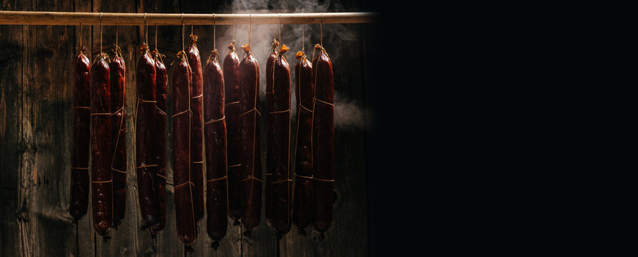 The process of smoking hanging sausages in the smokehouse. Clouds of smoke rise up and envelop the sausages hanging in a row. Long banner format