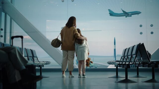Airport Terminal: Beautiful Mother and Cute Little Daughter Wait for their Vacation Flight, Looking out of Window for Arriving and Departing Airplanes. Young Family in Boarding Lounge of Airline Hub