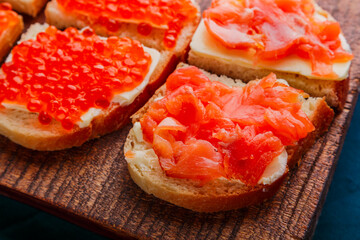 Bruschetta with red caviar and fish on a brown wooden board.