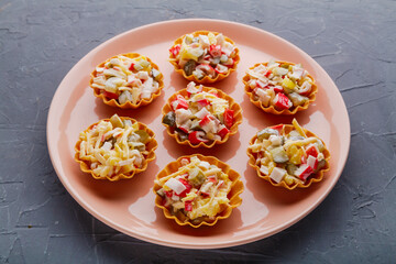 Salad with crab in tartlets on a beige plate on a black background.