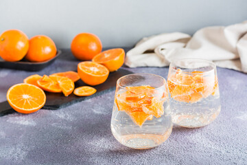 Non-alcoholic cocktail mineral water with pieces of tangerines in glasses and ripe fruits next to on the table. Detox food