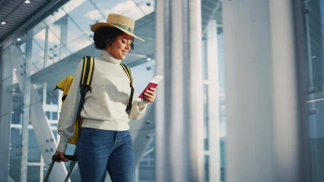 Airport Terminal: Beautiful Smiling Black Woman Holds Ticket, Walks Through in Airline Hub to the Gates Where Airplane Waits. Happy African American Female is Ready for Flight to Vacation Destination
