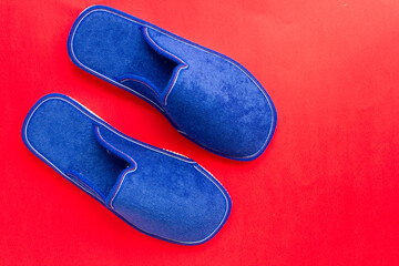 Blue house slippers on red background. Copy space.