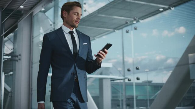 Airport Terminal: Businessman Walks to His Flight Gates, Uses Smartphone, Doing e-Business, Browsing the Internet with App. Digital Entrepreneur Remote Work Online While Traveling Through Airline Hub