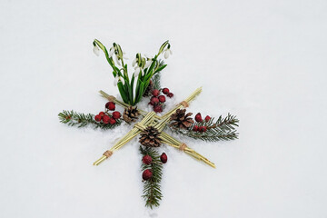 Brigid's cross, snowdrops flowers, fir branches, berries on snow background. symbol of Imbolc...