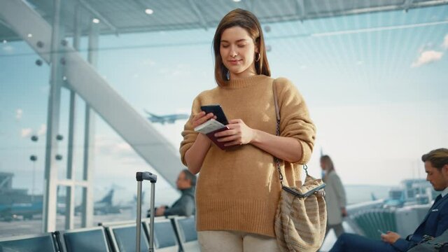 Airport Terminal: Happy Traveling Caucasian Woman Waiting at Flight Gates for Plane Boarding, Uses Mobile Smartphone, Checking Trip Destination on Internet. Smiling White Female on Vacation Trip