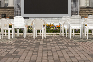 Open air cinema with group of white plastic chairs and black screen in summer day without people