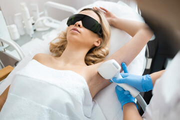 Beautyful blonde woman on underarm laser epilation procedure. Female doctor cosmetologist removes hair from the armpits of the patient