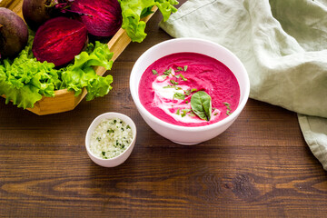 Red beet soup in white bowl with raw beet roots