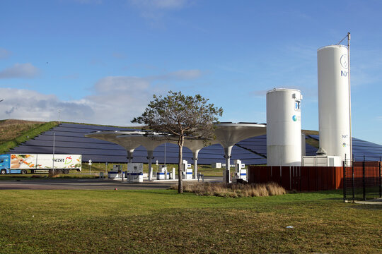 Dutch Petrol station with futuristic awning from NXT with a hill with solar panels in the background. A truck drives away. Tree, Gas storage tanks. Alkmaar, Netherlands, January