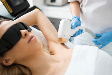 Laser epilation. Closeup of beautician hands removing hair of beautiful blonde woman's armpit