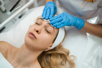 Professional beautician wipes female client's face with cotton pads and prepares her for cosmetic procedures. .Facial skin care concept