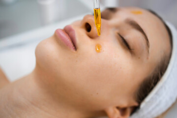 Close up of beautiful woman receiving nourishing oil treatment in beauty salon. Beautician holding pipette and applying serum on face of woman in spa salon