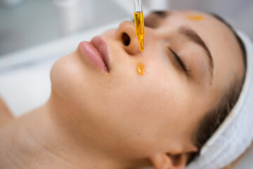 Close up of beautiful woman receiving nourishing oil treatment in beauty salon. Beautician holding...