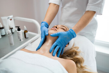Beautician giving relaxing face and neck massage to young woman. Relaxed woman enjoys a face and neck massage at a spa