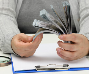 a stack of one hundred dollar bills in a woman's hand and a wooden magnifying glass on a white...