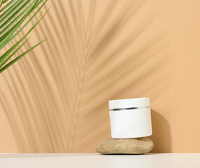 white round plastic jar for cosmetic products on a brown background. Palm leaf shadow. Blank for branding products, mock up