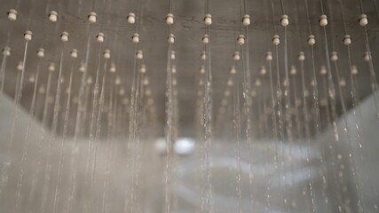 Shower in the bathroom from which water begins to pour. Close up of Water flowing from shower. Stylish square shower head that starts pouring water.