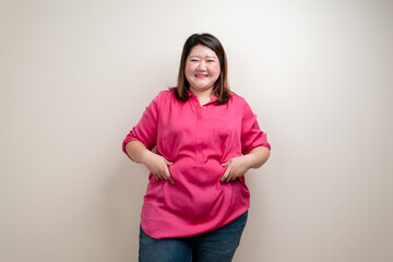 Fototapeta premium Fat woman pink shirt, Obese woman hand holding excessive belly fat isolated on clean background, Overweight fatty belly of woman diet lifestyle overweight Happy and self-esteem concept.