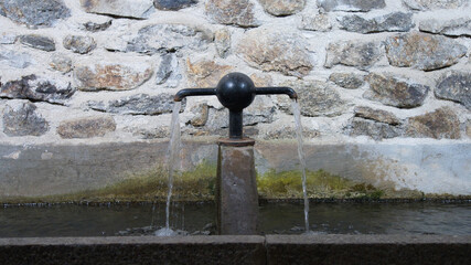 Close up of a metal and stone village fountain, water flowing from the taps in two directions