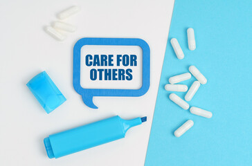 On a white and blue table are pills, a marker and a blue plaque with the inscription - CARE FOR OTHERS