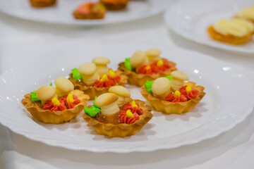 Assortment of delicious fresh shortcrust tart cakes with cream and sweet mushrooms on white plate for sale at restaurant, cafe - close up. Dessert, culinary and confectionery concept