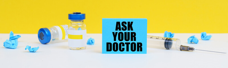 On the table is a syringe, injections and a blue sign with the inscription - ASK YOUR DOCTOR
