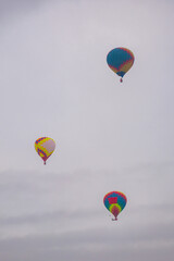 Three colorful hot air balloons flying against grey sky at Winter aerostat festival. Freedom, sport, aircraft concept