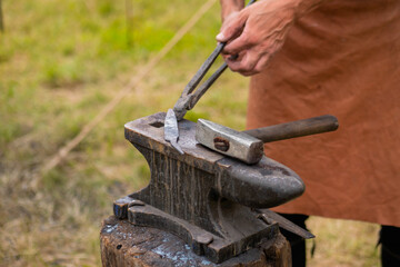 Professional blacksmith working with metal on anvil at outdoor workshop - close up view, selective...